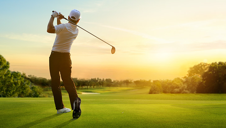 Golfer striking ball facing a sunset